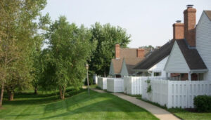 White apartment with a white picket fence, brick chimneys, and green grass