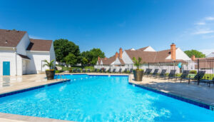 Bright blue swimming pool on a summer day next to white Pinegate West apartment buildings.